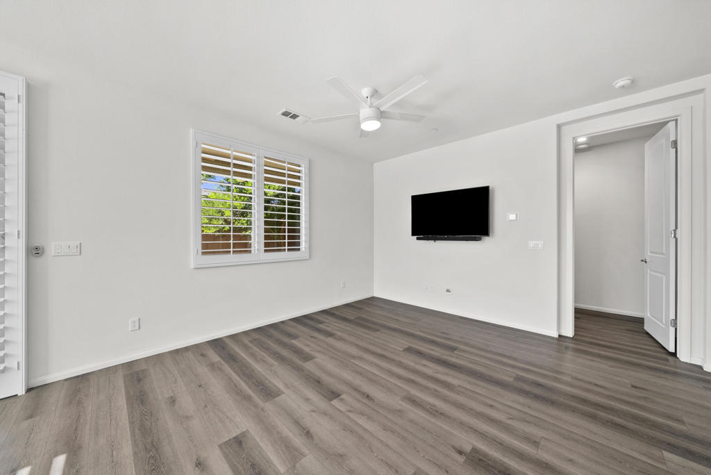 Empty room with gray wood-look flooring, a ceiling fan, and a wall-mounted TV.