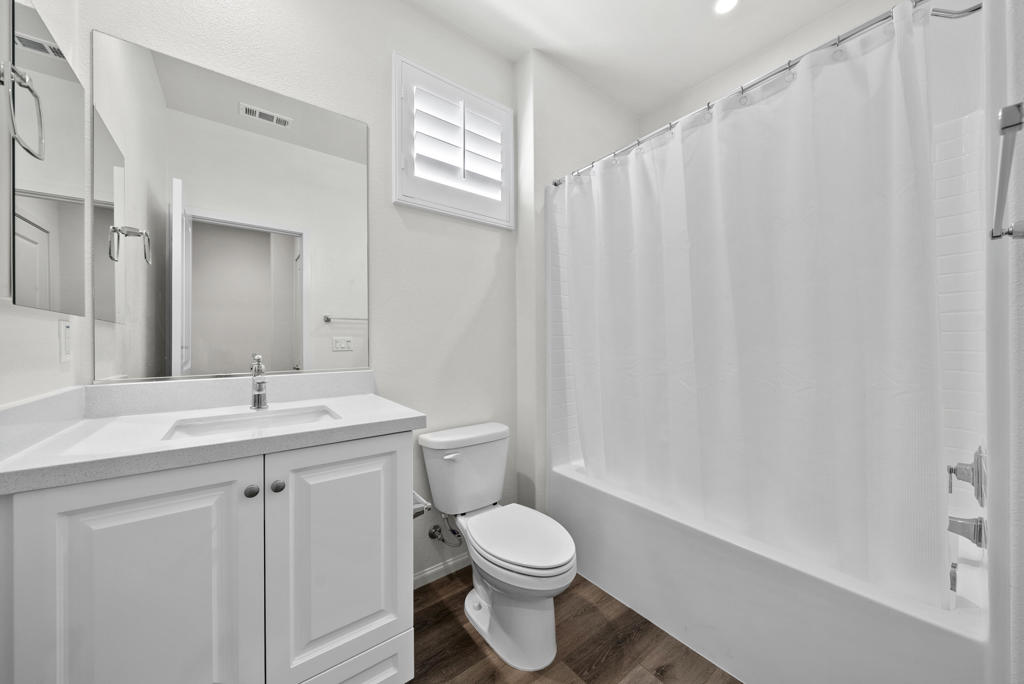 Bathroom with a white vanity, toilet, and tub behind a shower curtain.
