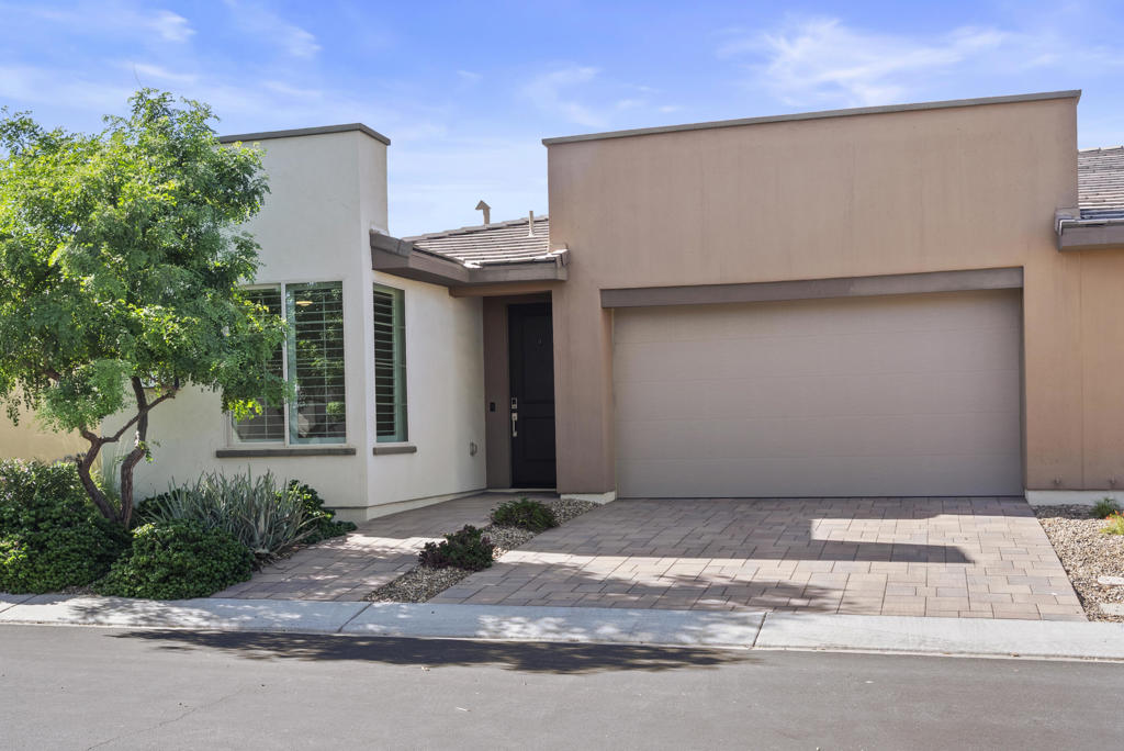 Modern stucco home with a two-car garage, paver driveway, and desert landscaping.