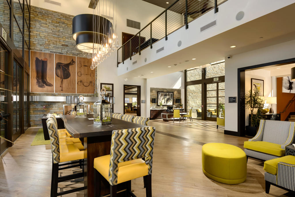Dining and lounge area with a long table, yellow-accented seating, stone walls, and a mezzanine.