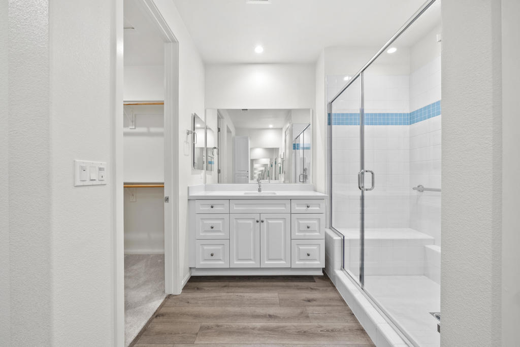 Bathroom with a white double vanity, glass-enclosed shower, and blue tile accent.