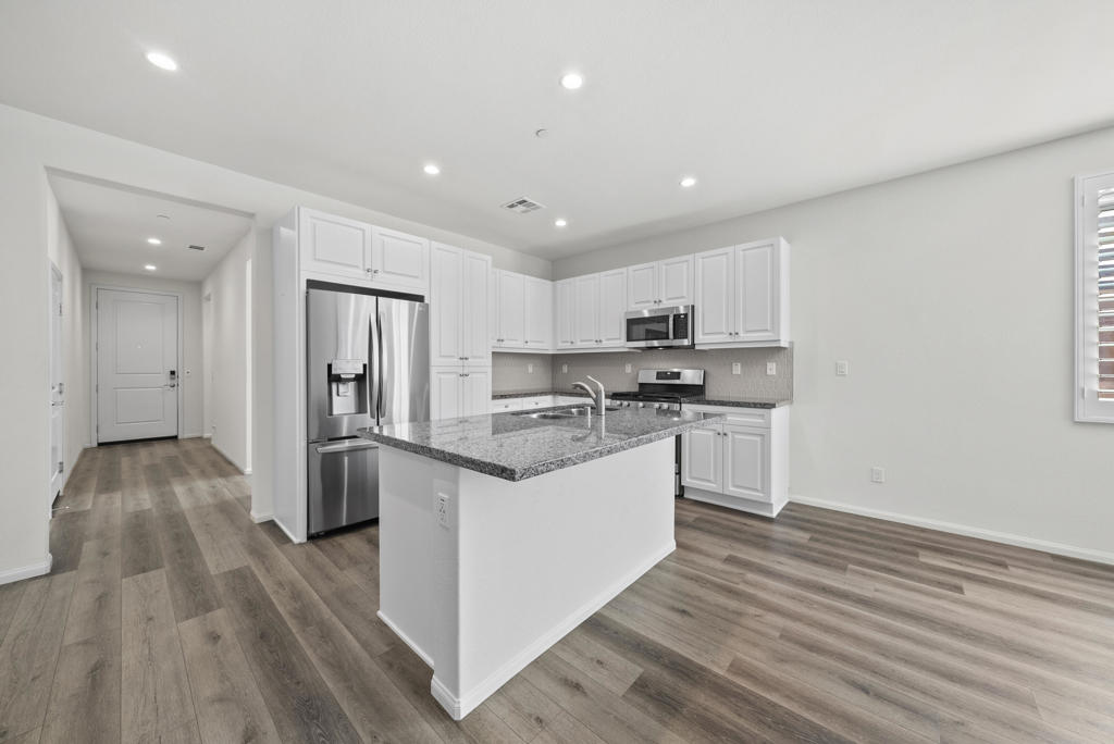 Kitchen with a granite island, stainless steel appliances, and white cabinetry.