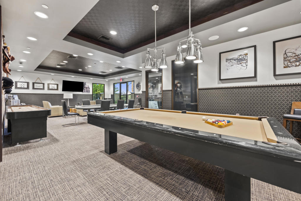 Billiard room with two pool tables, lounge seating, and modern pendant lights.