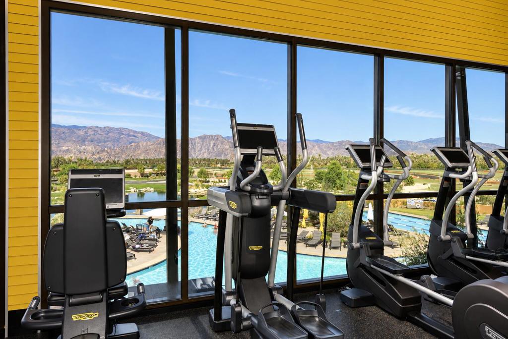 Fitness center with cardio machines overlooking a swimming pool and mountains.