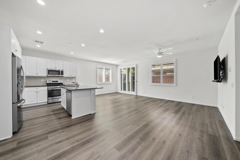 Open kitchen and living area with white cabinets, stainless steel appliances, and wood-look flooring.