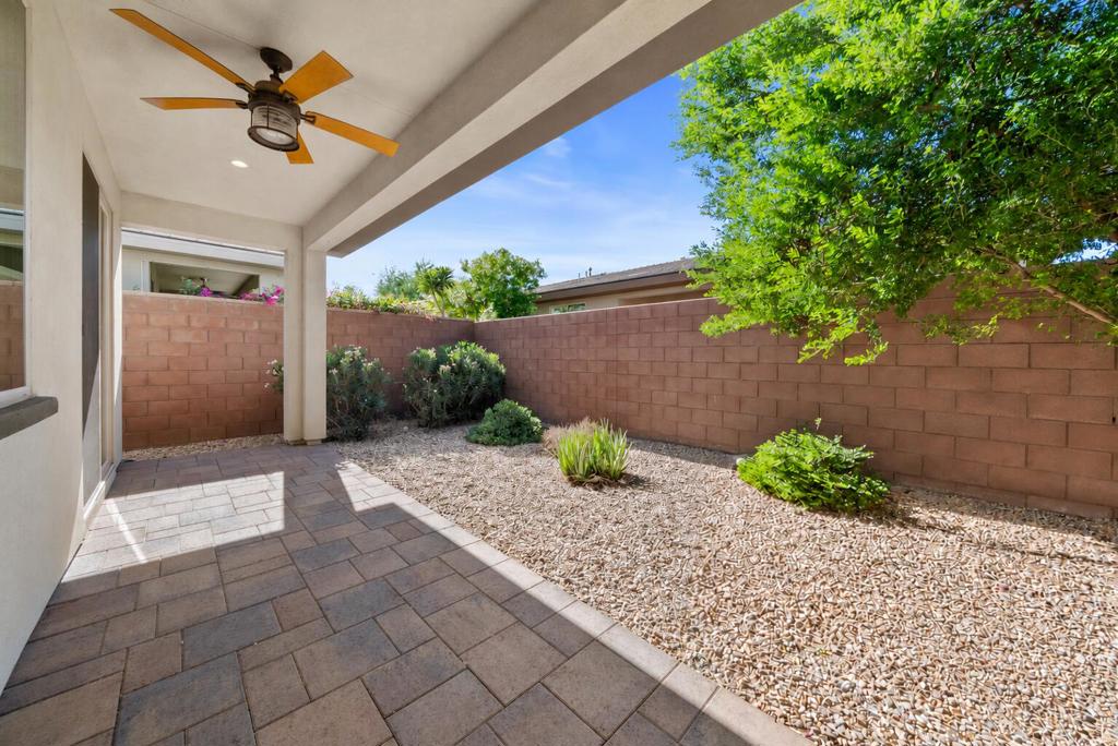 Covered patio with paver flooring, a ceiling fan, and a gravel yard enclosed by a block wall.