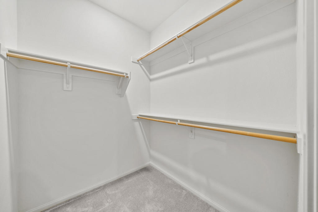 Walk-in closet with white shelving, wooden hanging rods, and light carpet.