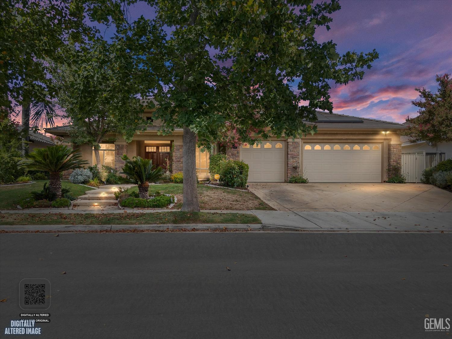 Single-story home with stone accents and a two-car garage beneath mature trees at dusk.