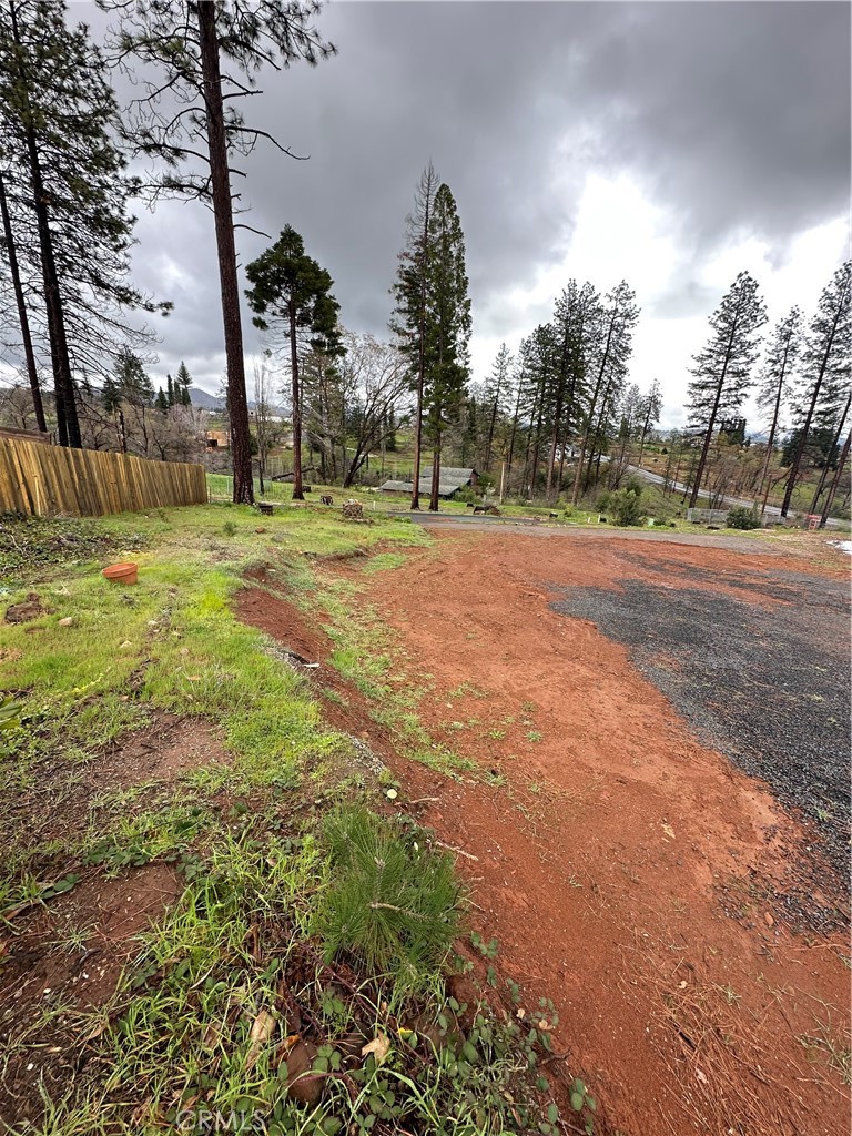 Vacant wooded lot with a broad red-dirt clearing and wooden fence.