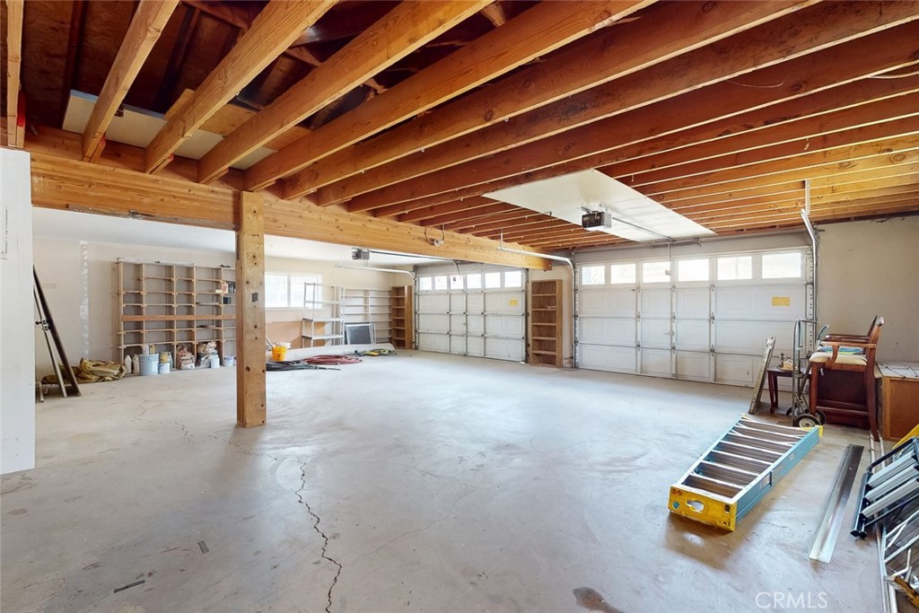 Large garage with exposed wooden ceiling joists, multiple doors, and a concrete floor.