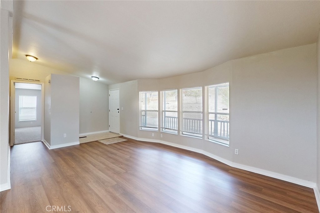 Empty living room with wood-look flooring and a row of windows overlooking a deck.