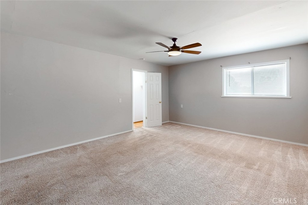 Empty bedroom with beige carpet, a ceiling fan, and a window with blinds.