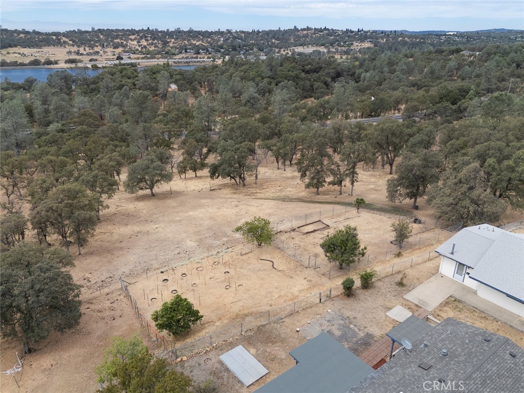 Aerial view of fenced, oak-dotted grounds with a play area, nearby house, and distant water.