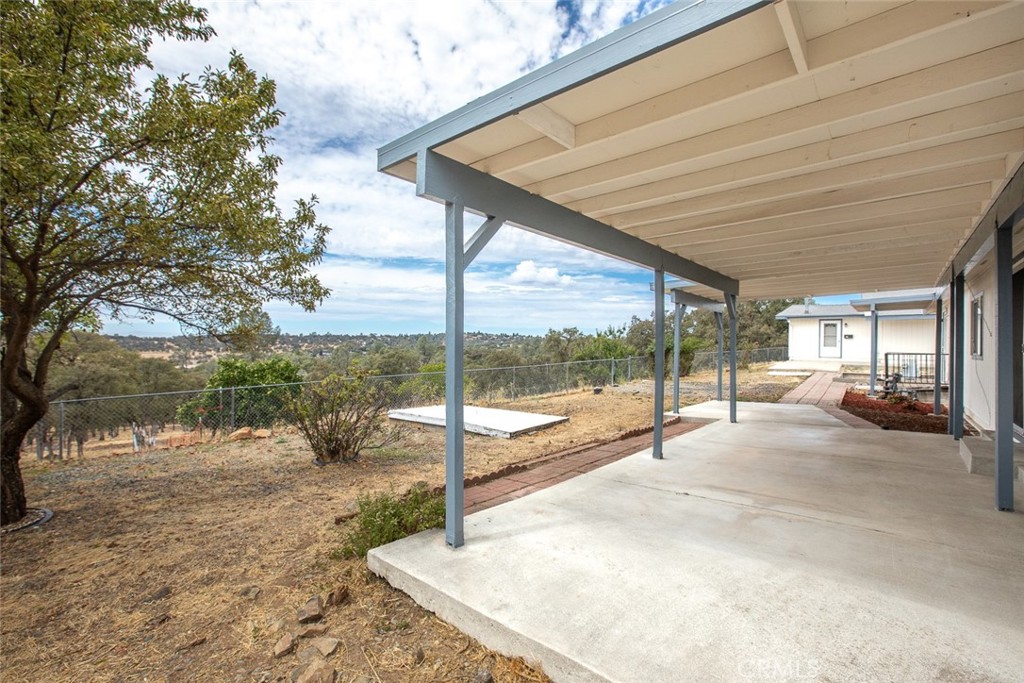 Covered concrete patio overlooking a fenced, tree-dotted hillside.
