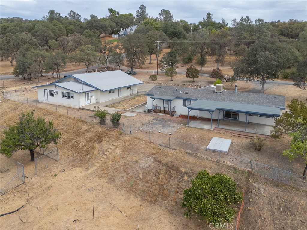 Aerial view of two homes on a fenced rural lot with dry ground and wooded hills.