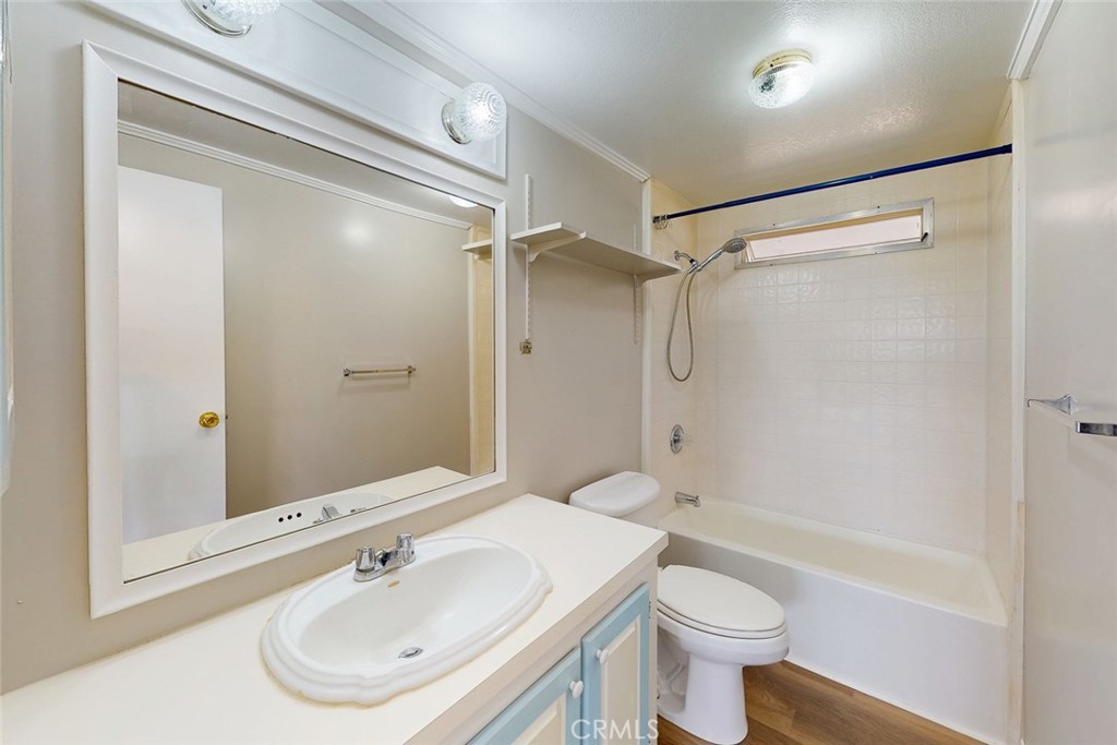 Bathroom with a white tub and shower, toilet, and vanity beneath a large framed mirror.