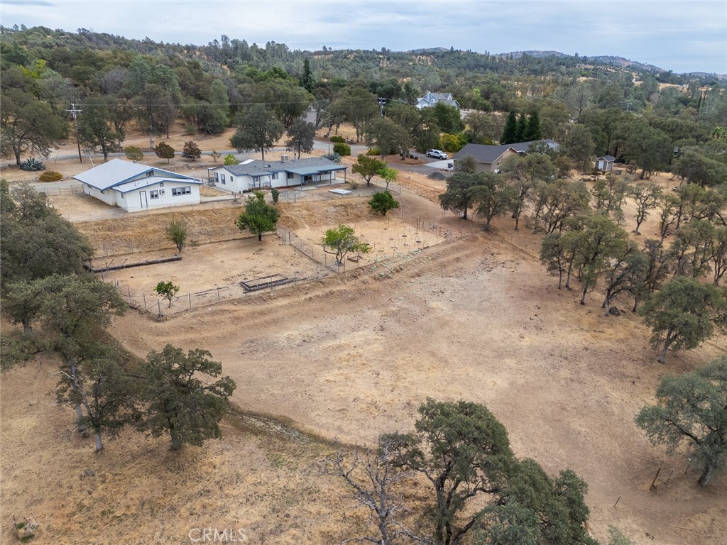 Aerial view of homes and fenced acreage among dry, oak-dotted hills.