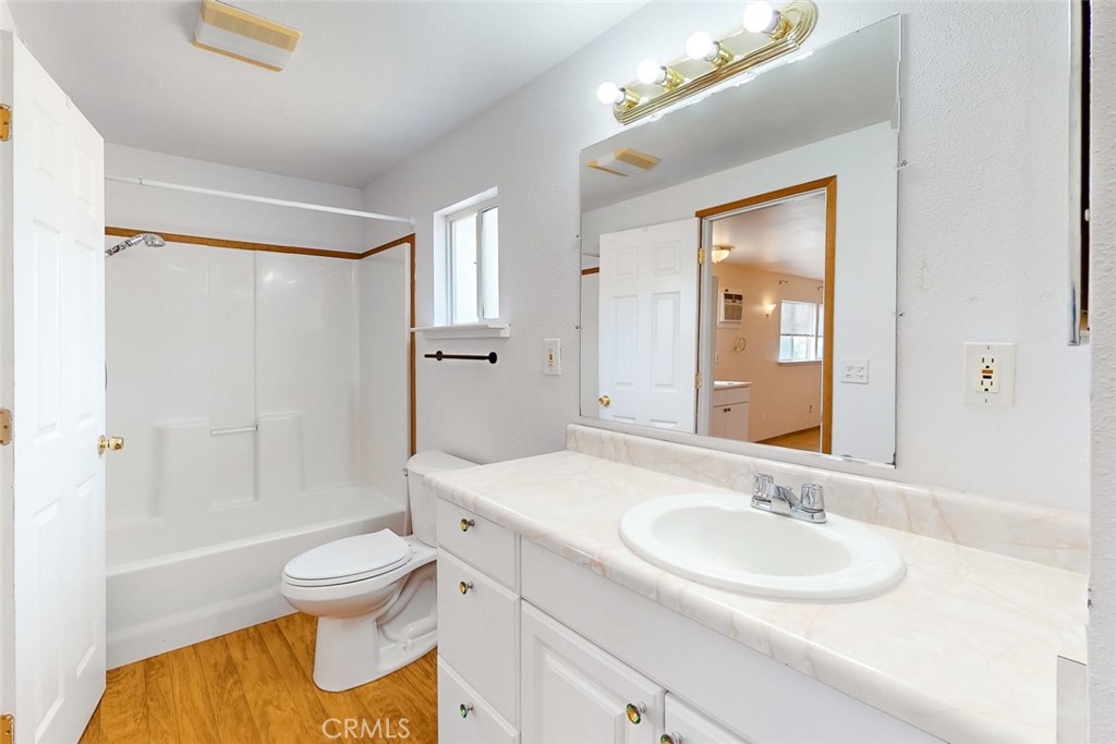 Bathroom with a white tub and shower, toilet, and long vanity with a large mirror.