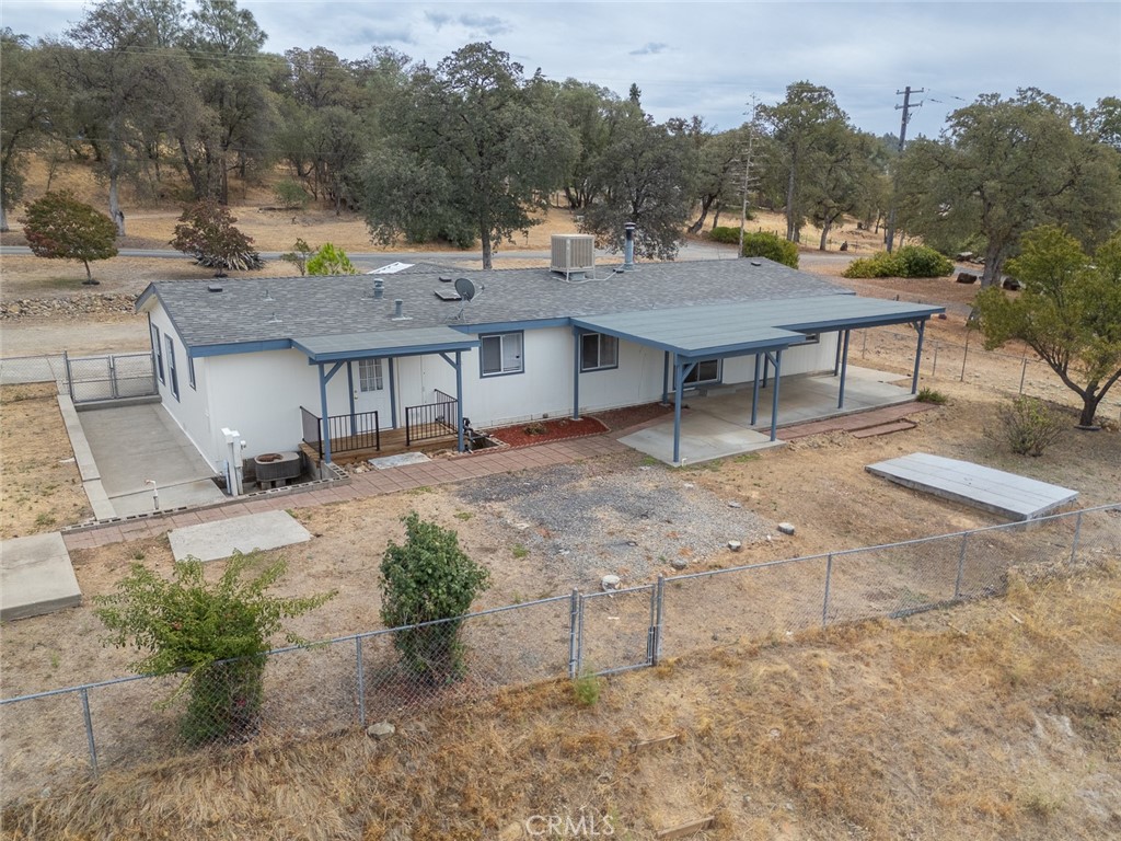 Single-story white home with blue trim and a long covered carport on a fenced rural lot.