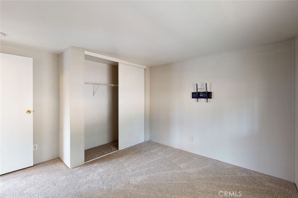 Empty bedroom with beige carpet, an open sliding-door closet, and a wall-mounted TV bracket.
