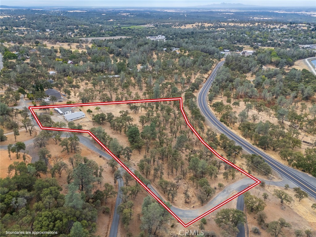 Aerial view of a rural parcel outlined in red, with scattered trees, a small house, and nearby roads.