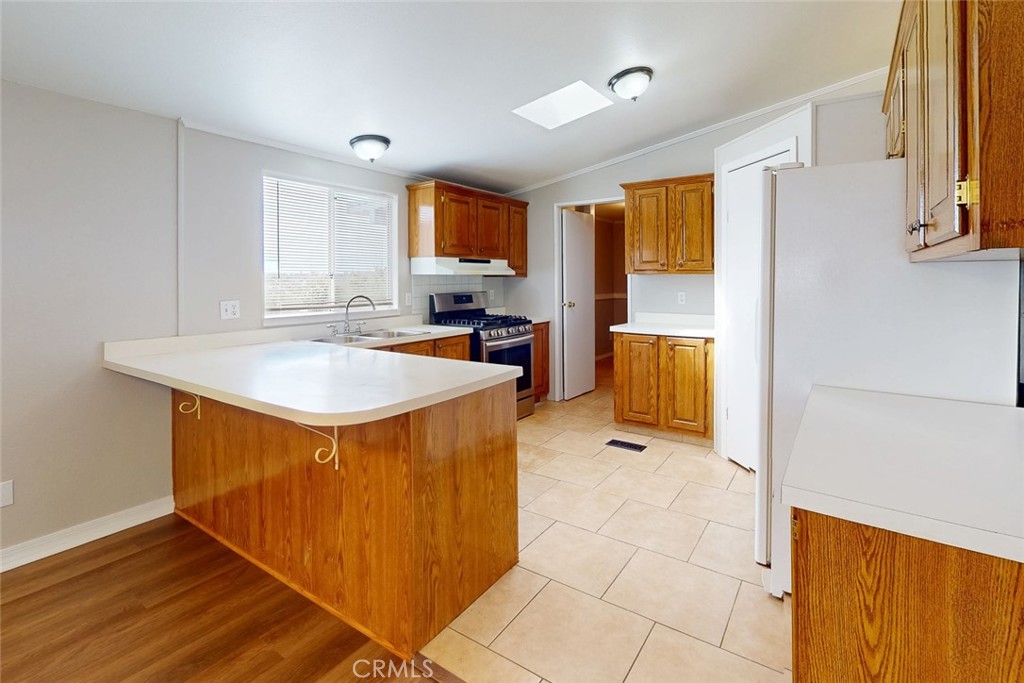 Kitchen with a large white peninsula, honey-colored wood cabinets, gas range, and beige tile floor.