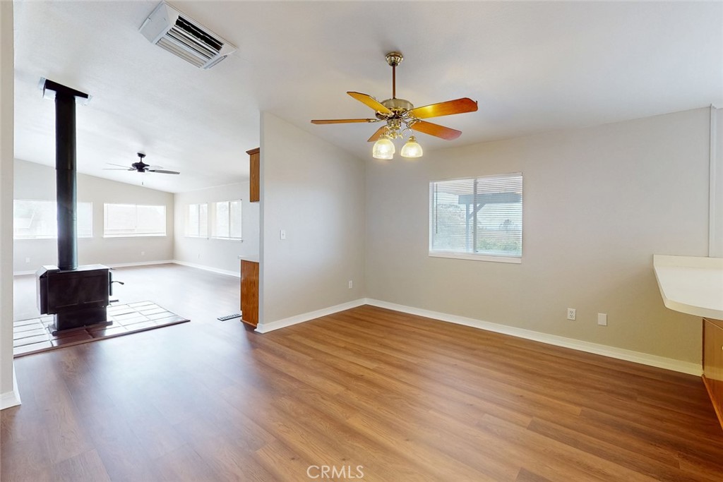 Vacant open living and dining area with wood floors and a wood-burning stove.