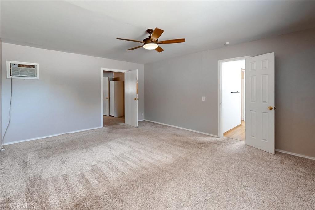 Empty carpeted bedroom with a ceiling fan, window air conditioner, and two open doorways.