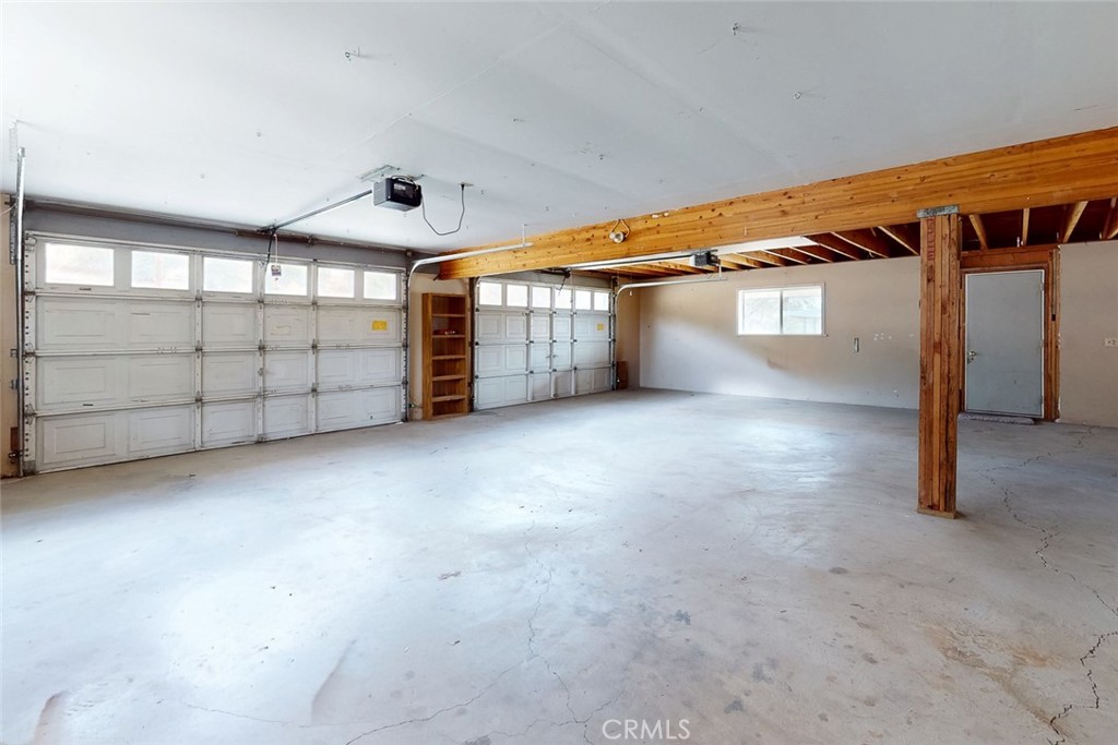 Vacant garage with two sectional doors, exposed wooden beams, and a concrete floor.