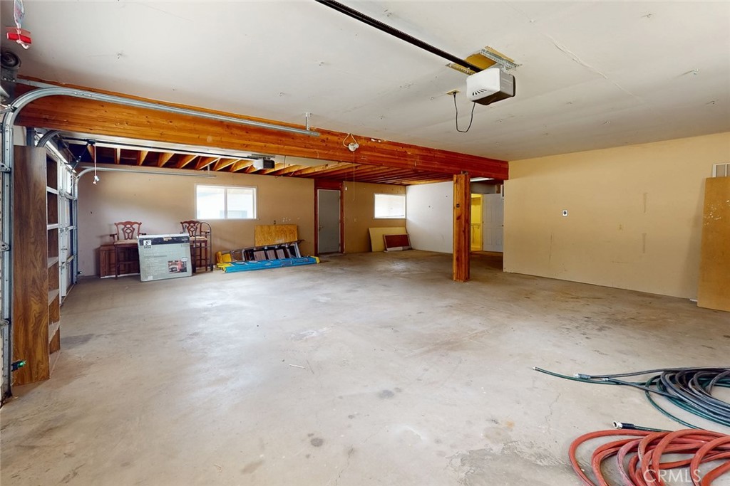 Large garage with a concrete floor, exposed wooden beams, and an open overhead door.