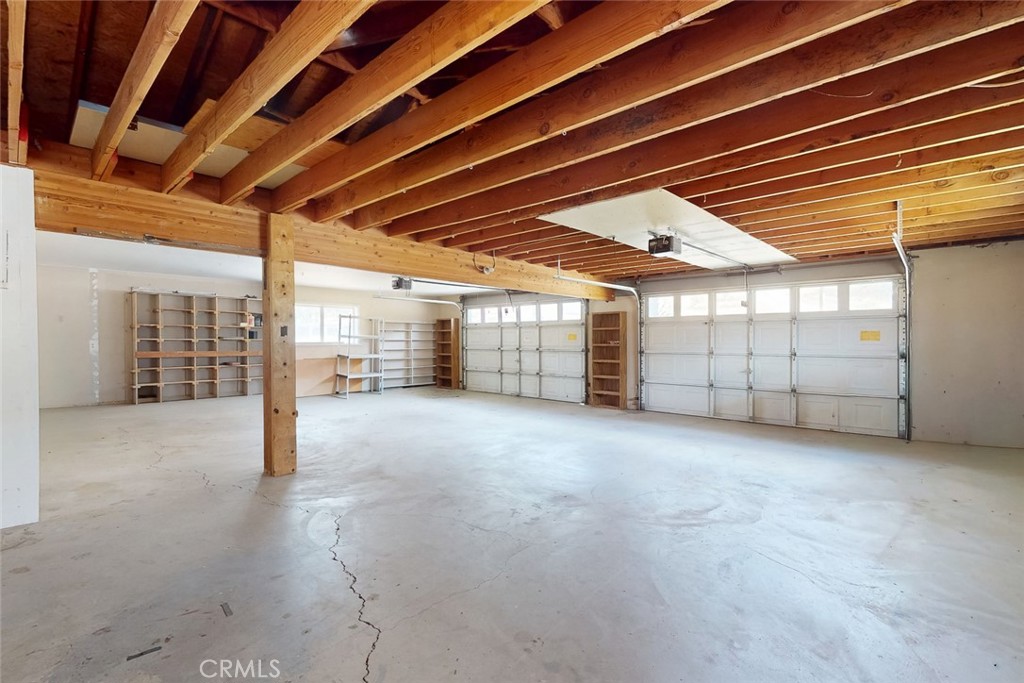 Spacious garage with exposed wood ceiling beams, built-in shelving, and two white garage doors.