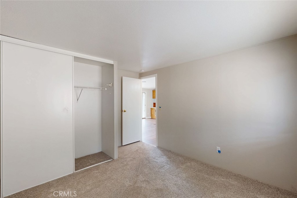 Vacant bedroom with beige carpet, an open sliding-door closet, and a doorway to another room.