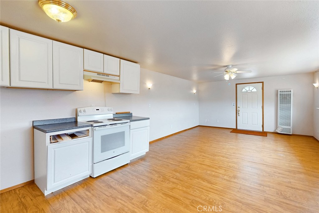 Vacant kitchen with white cabinets and electric range opening onto a wood-look-floored living area.