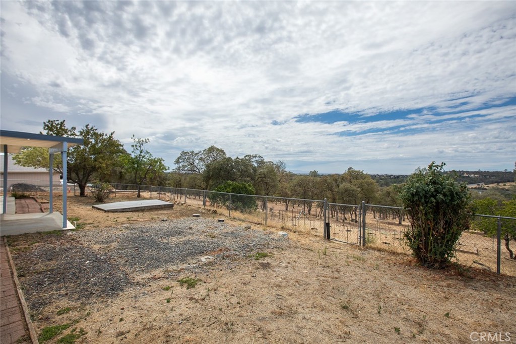 Fenced yard with a covered patio, gravel landscaping, and distant rolling hills.