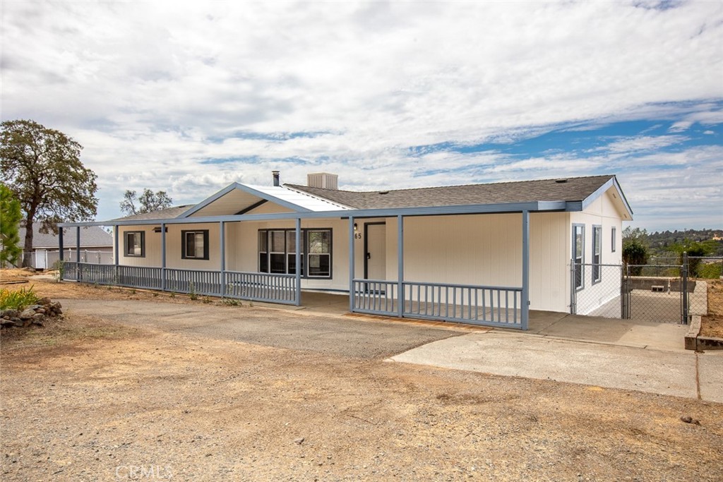 Single-story home with blue-gray trim, a long covered porch, and a broad gravel driveway.