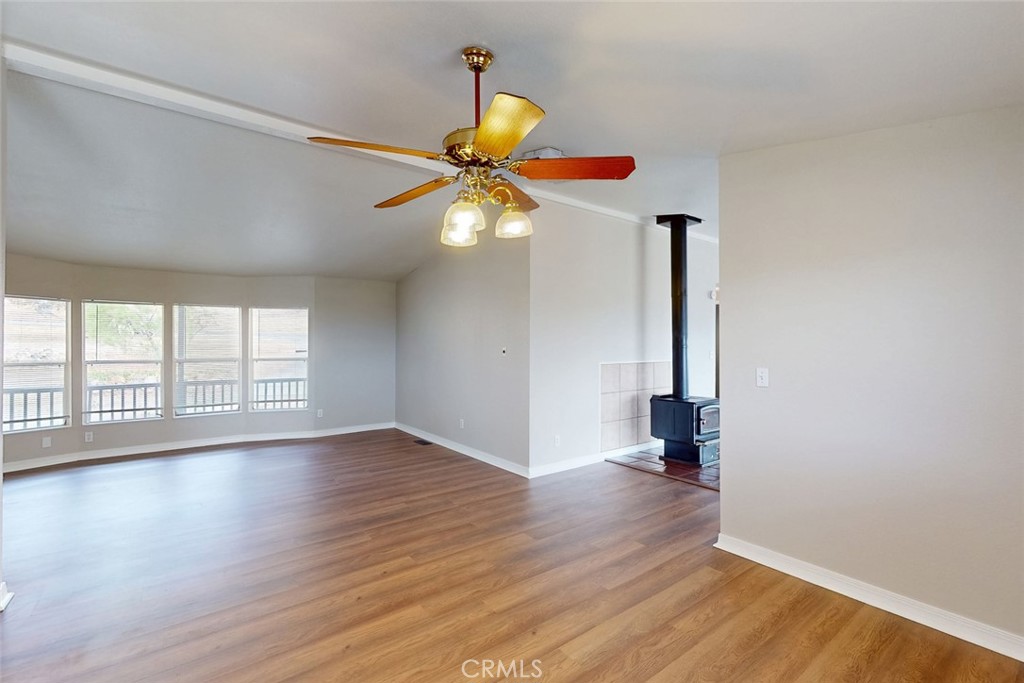Empty living room with wood-look floors, large windows, and a black wood-burning stove.