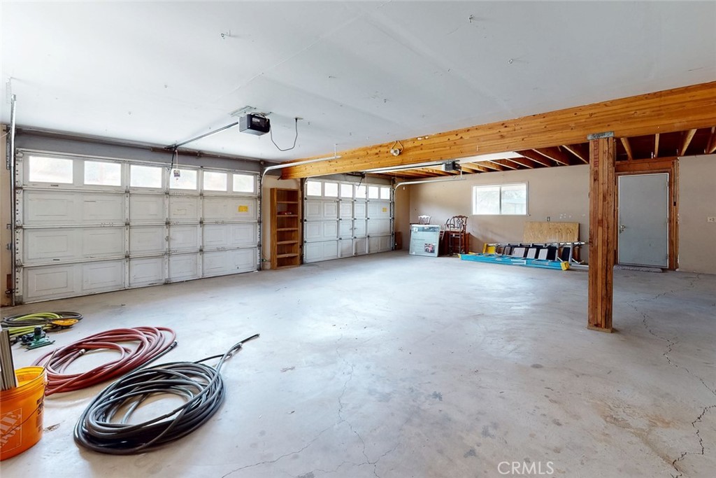 Spacious garage with two large doors, exposed wooden beams, and coiled hoses on the concrete floor.