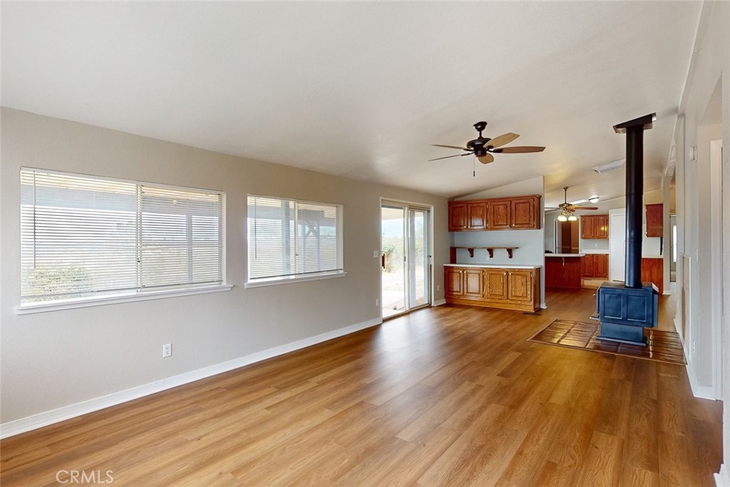Unfurnished living room with wide windows, wood-look flooring, and a freestanding wood stove opening to the kitchen.