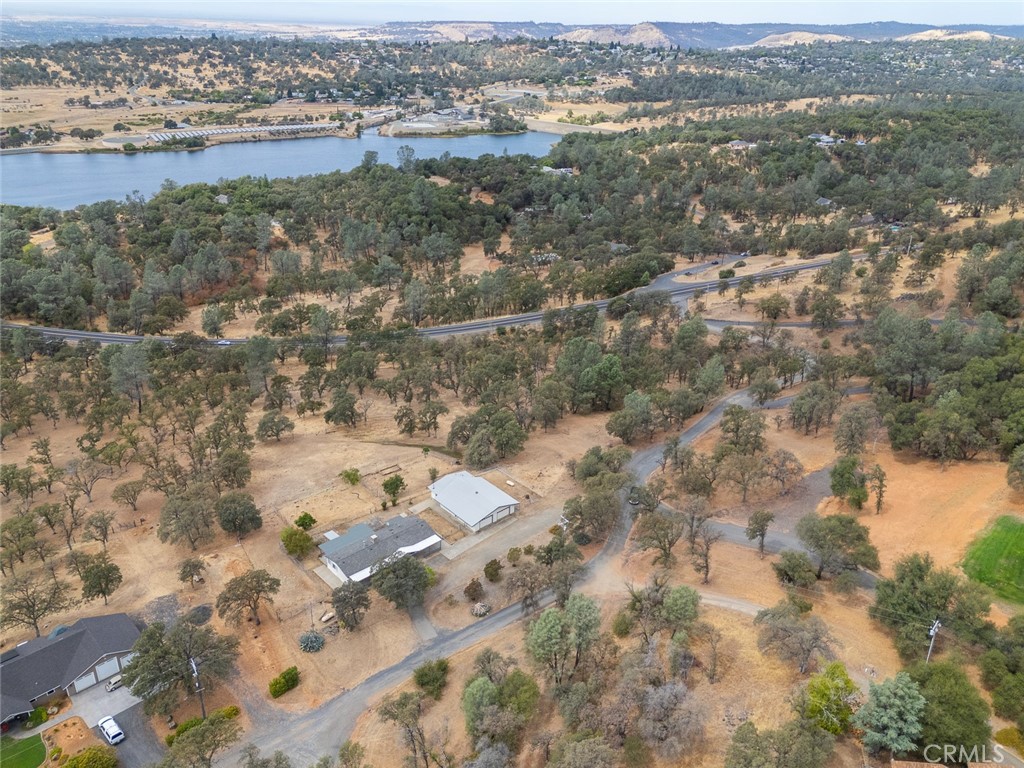 Aerial view of wooded acreage with several buildings, winding roads, and water in the distance.