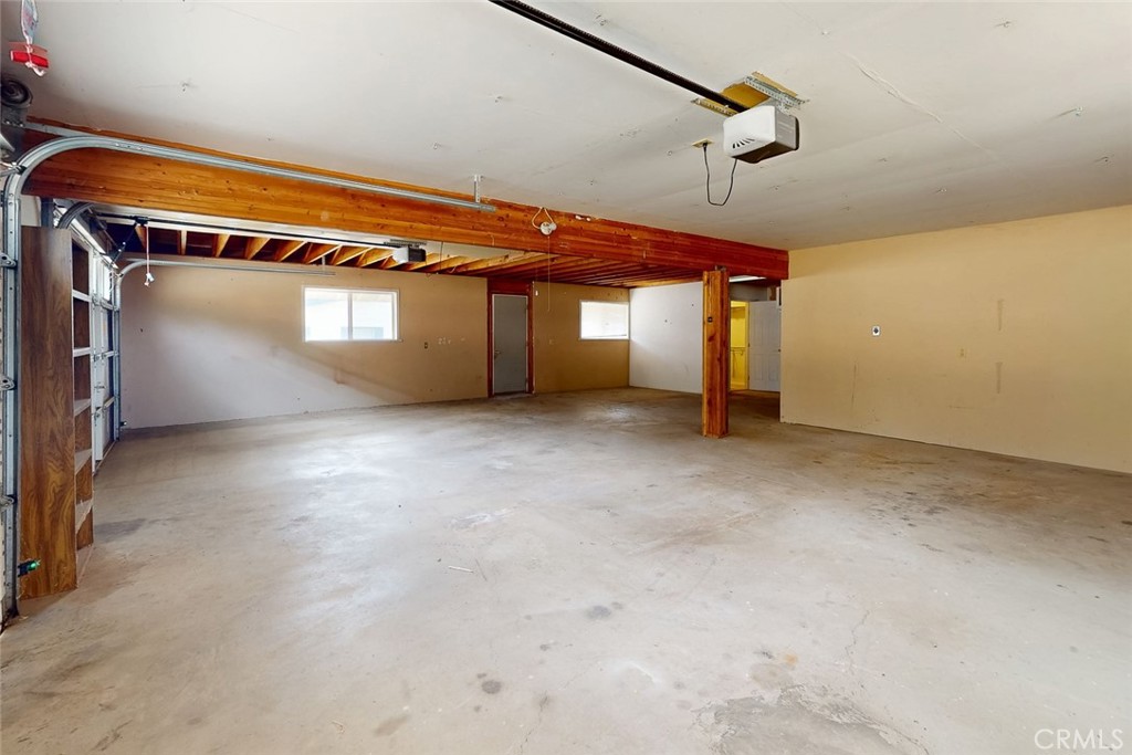 Empty garage with a concrete floor, exposed wooden beams, and an open garage door.