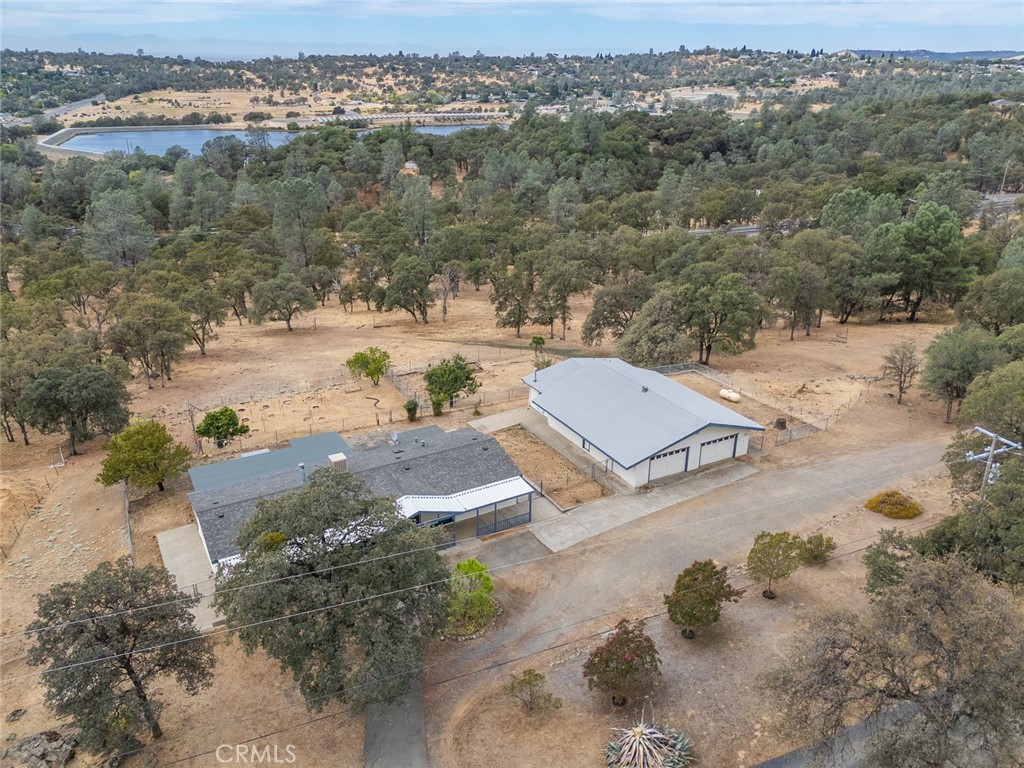 Aerial view of two buildings on dry, tree-covered land, with a reservoir in the distance.