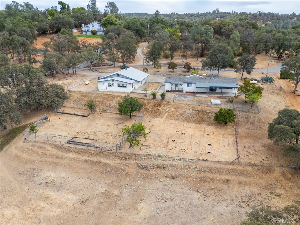 Aerial view of two white buildings and fenced dry land among scattered oak trees.