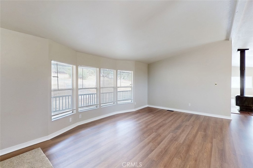 Unfurnished living room with wood-look floors, four windows, and a wood-burning stove at right.