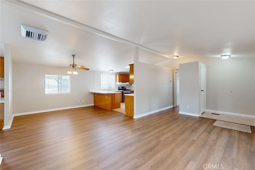 Open living area with wood-look flooring, ceiling fan, and adjoining kitchen with wood cabinets.