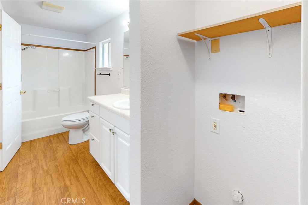Vacant bathroom with white tub and vanity beside a wall with a shelf and utility connections.