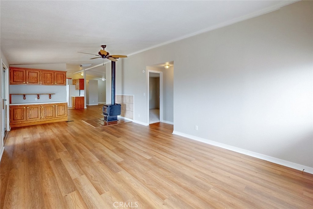 Open living area with wood-look flooring, wooden kitchen cabinets, and a freestanding wood stove.