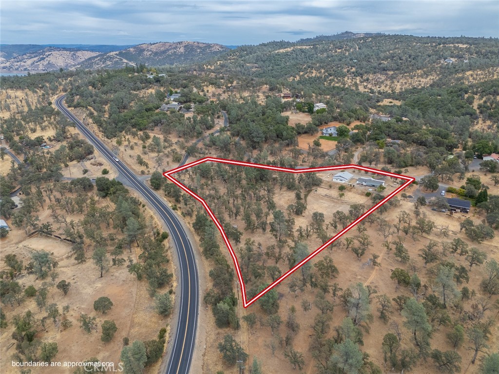 Aerial view of a rural, tree-dotted property outlined in red beside a winding road.