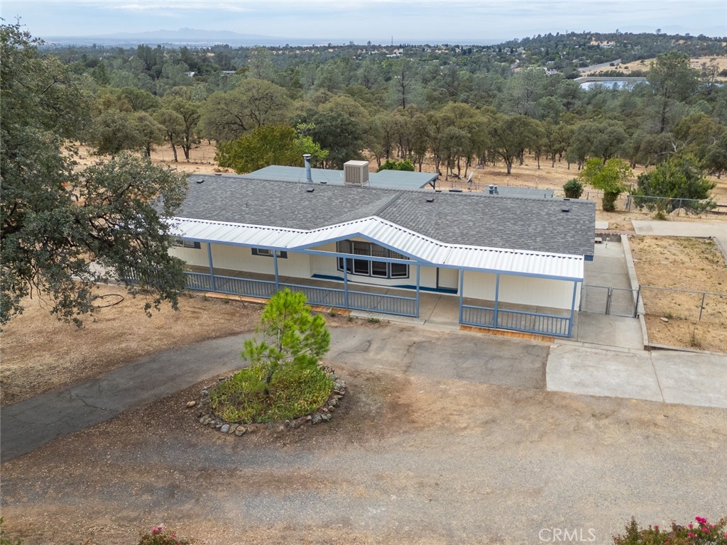 Single-story home with a long covered porch, blue railings, and dry wooded surroundings.
