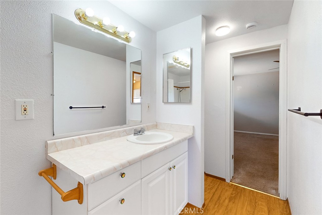 Bathroom with white vanity, marble-look counter, large mirror, and doorway to a carpeted room.