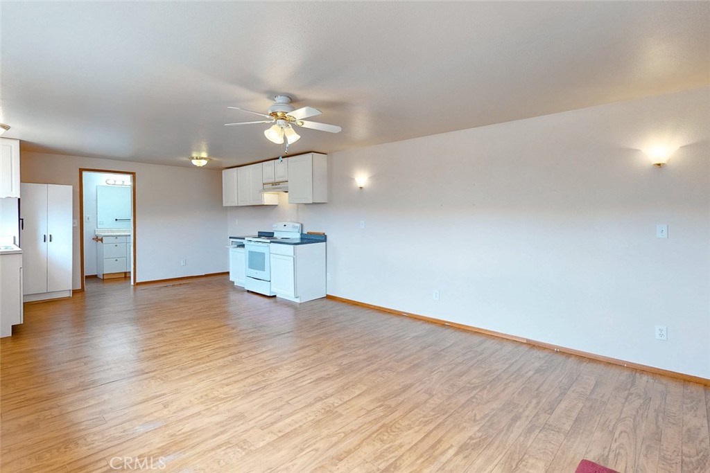 Vacant living area with wood-look floors, ceiling fan, and compact kitchen.